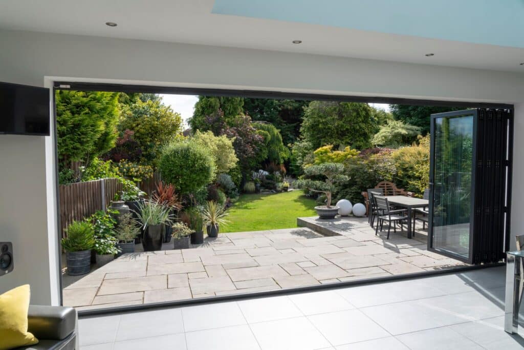 Schöner Garten und Patio im Sommer, Blick durch Flügeltüren auf Terrasse.