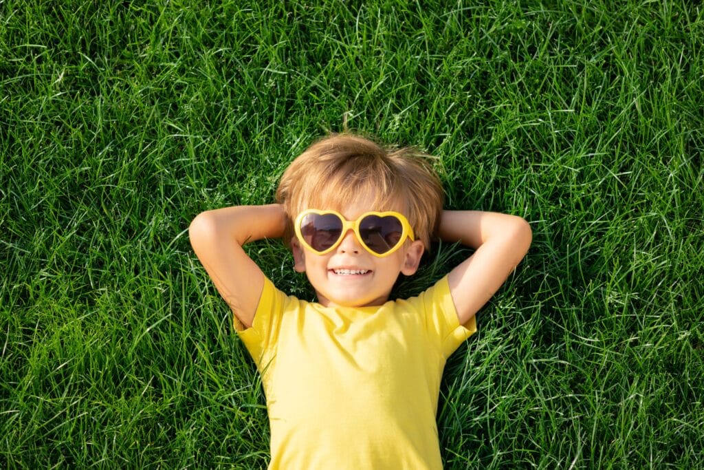 Ein Junge mit einer gelben Sonnenbrille liegt im Gras