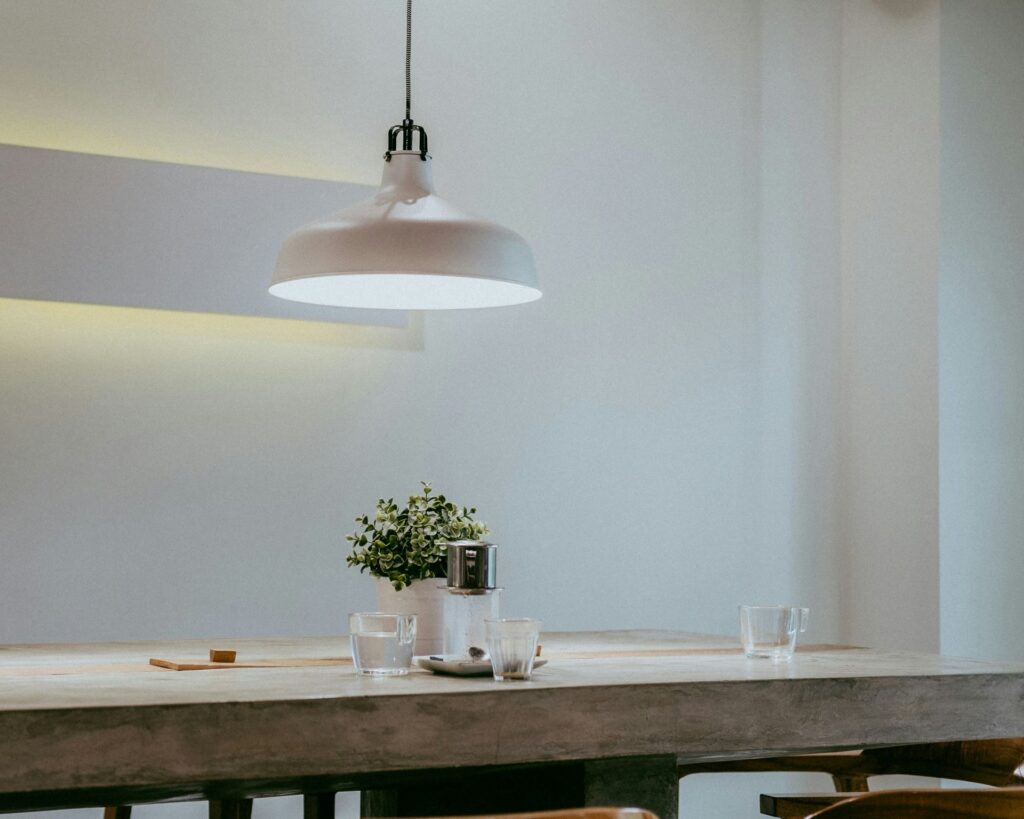 Minimalistisch gestalteter Essbereich mit einer Hängelampe über einem Holz-Esstisch, dekoriert mit einem kleinen Blumentopf und Glasgefäßen.