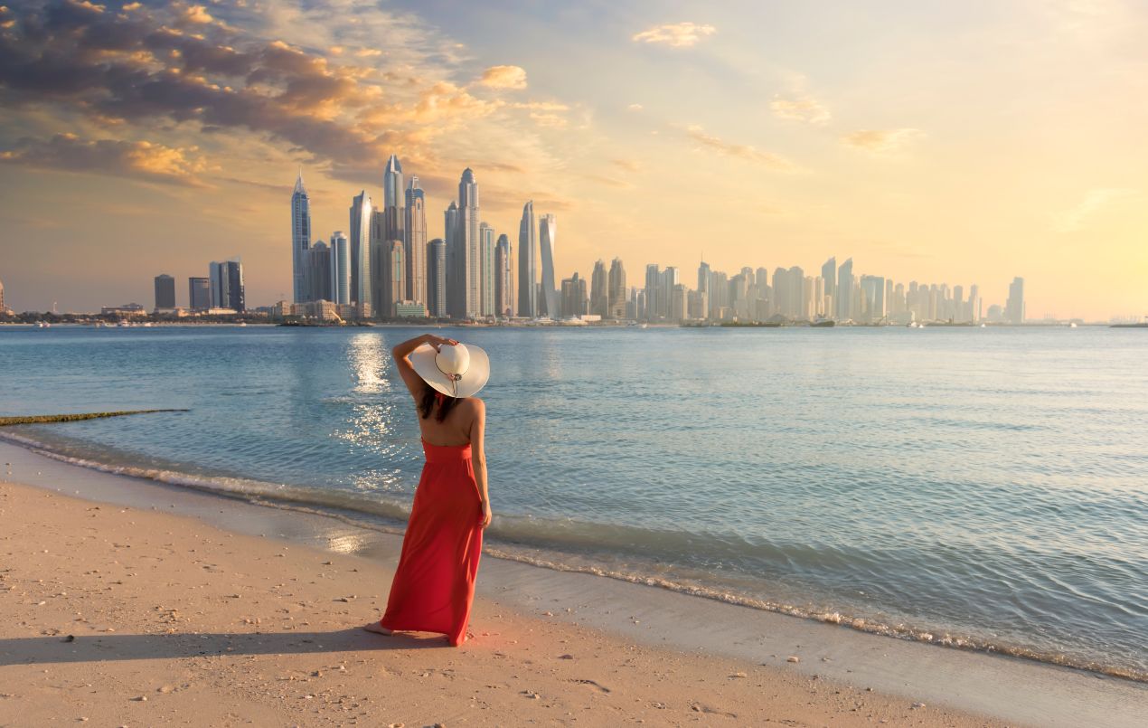 Frau am Strand mit Blick auf Dubais Skyline im Abendlicht – emotionaler Moment zum Thema Ferienhaus Dubai kaufen
