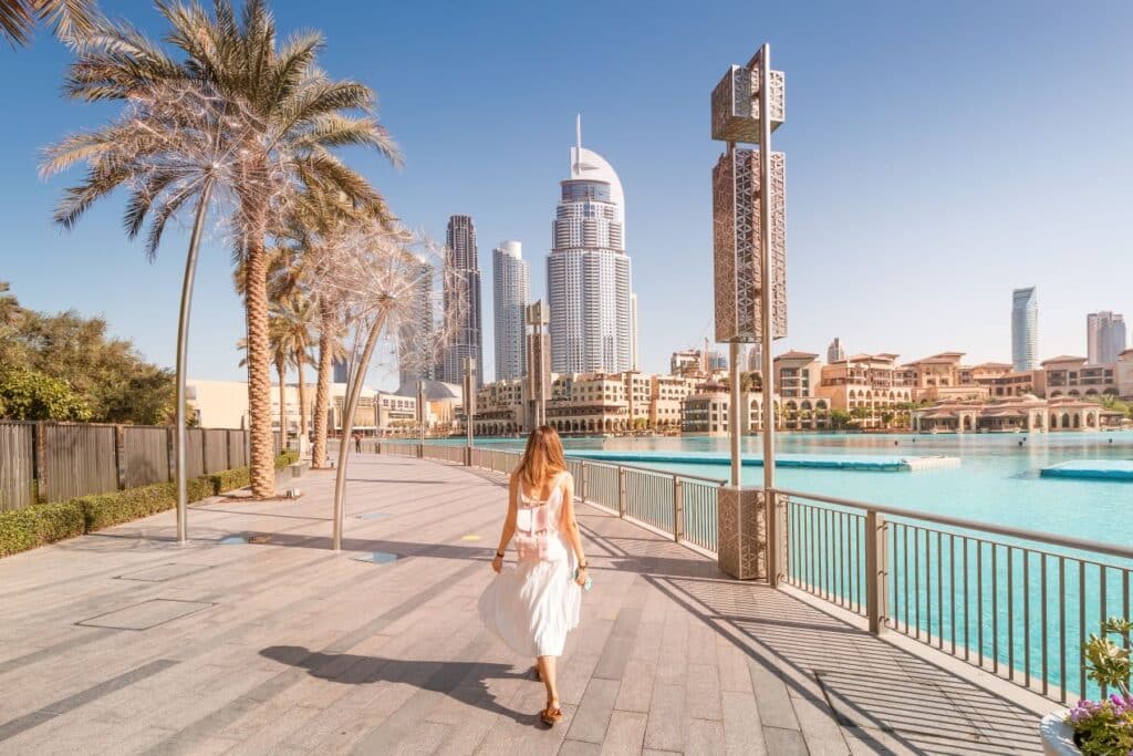 Frau spaziert entlang der Dubai Fountain mit Blick auf moderne Hochhäuser – idealer Eindruck für alle, die ein Ferienhaus Dubai kaufen wollen