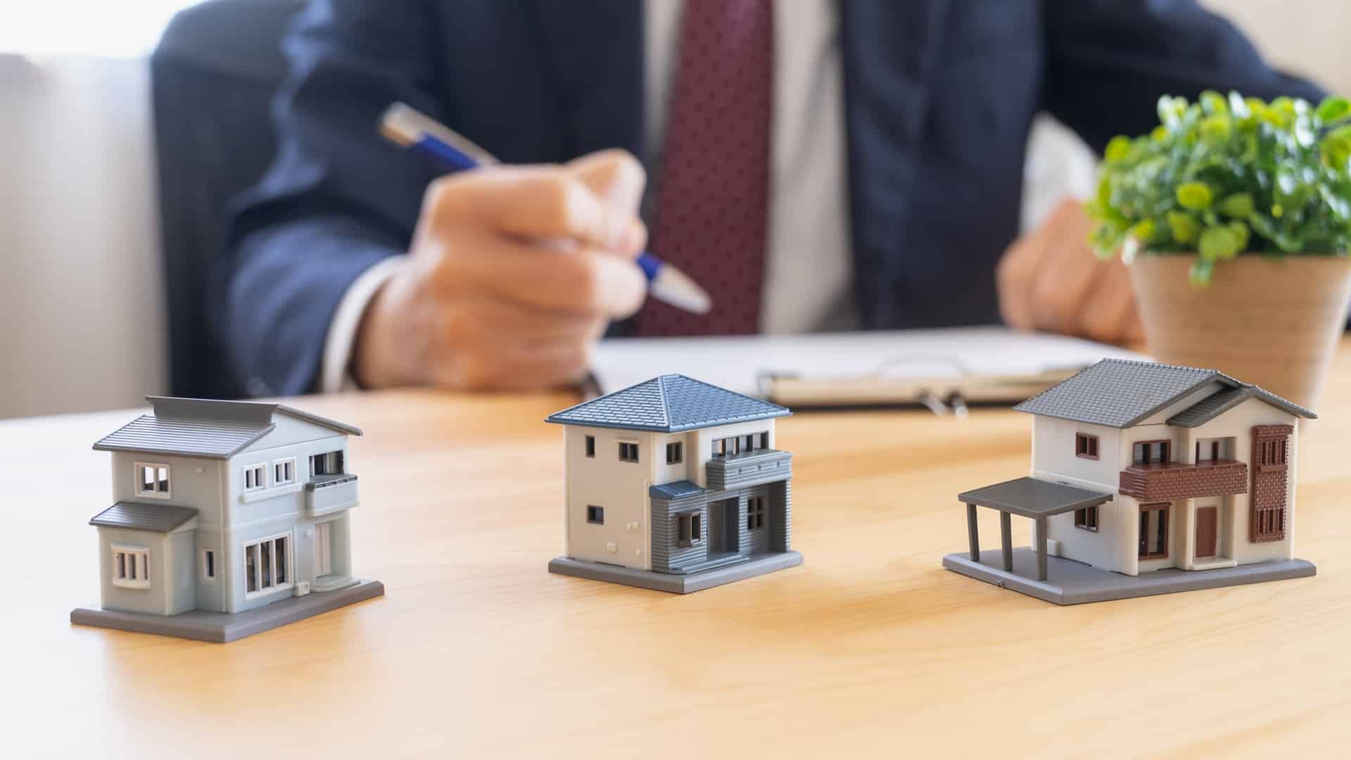 Drei Hausmodelle vor Berater am Schreibtisch | Immobilienfinanzierung Duisburg
